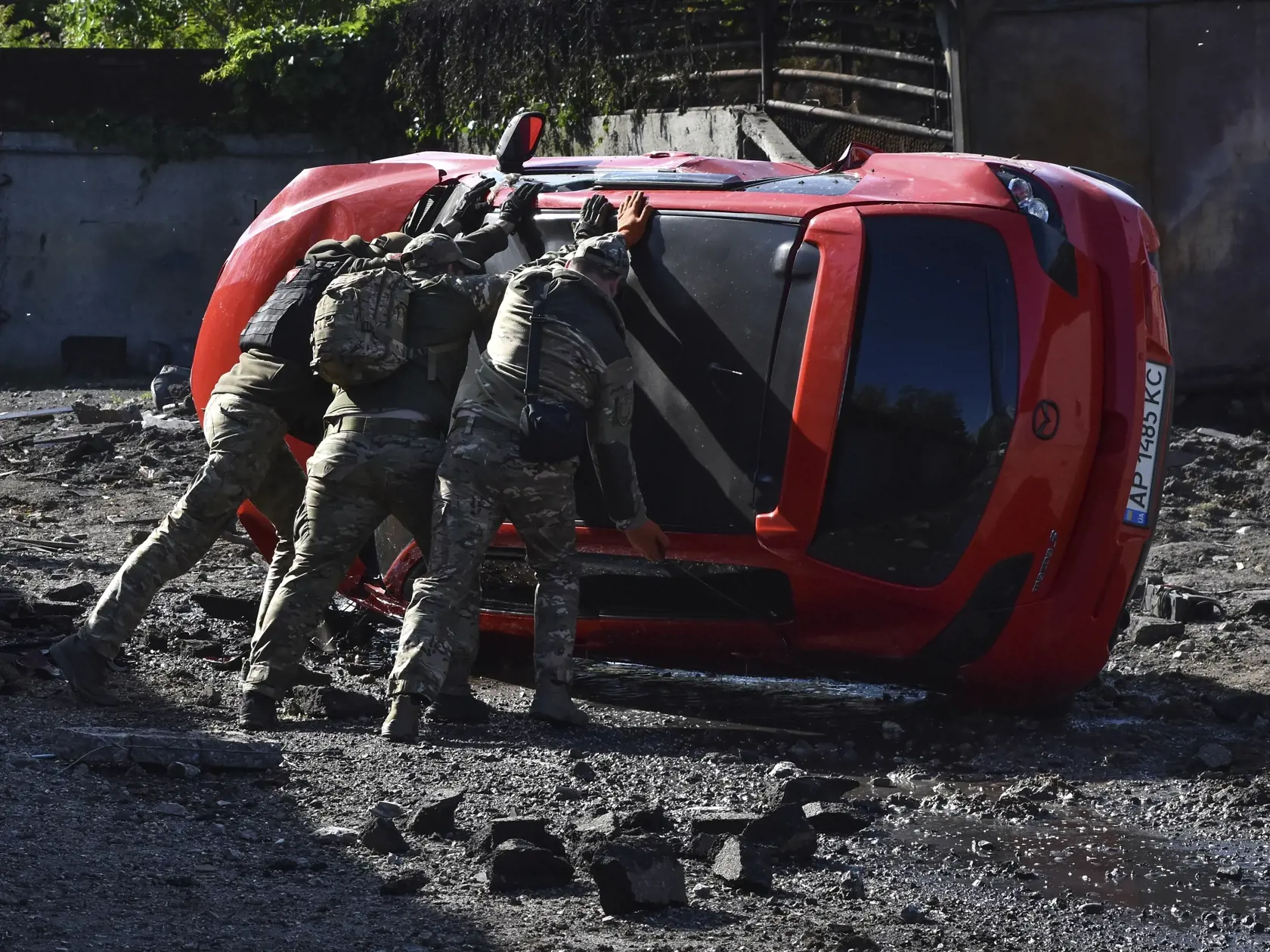Ukrajinskí vojaci otáčajú poškodené auto na mieste ruského raketového útoku v Záporoží 8. mája 2024.