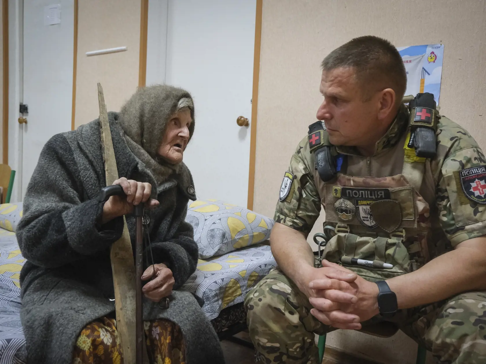 Na snímke 98-ročná starenka Lydia Stepanivnová sa rozpráva s policajtom v úkryte po úteku z územia okupovaného Ruskom v Doneckej oblasti na Ukrajine 26. apríla 2024.