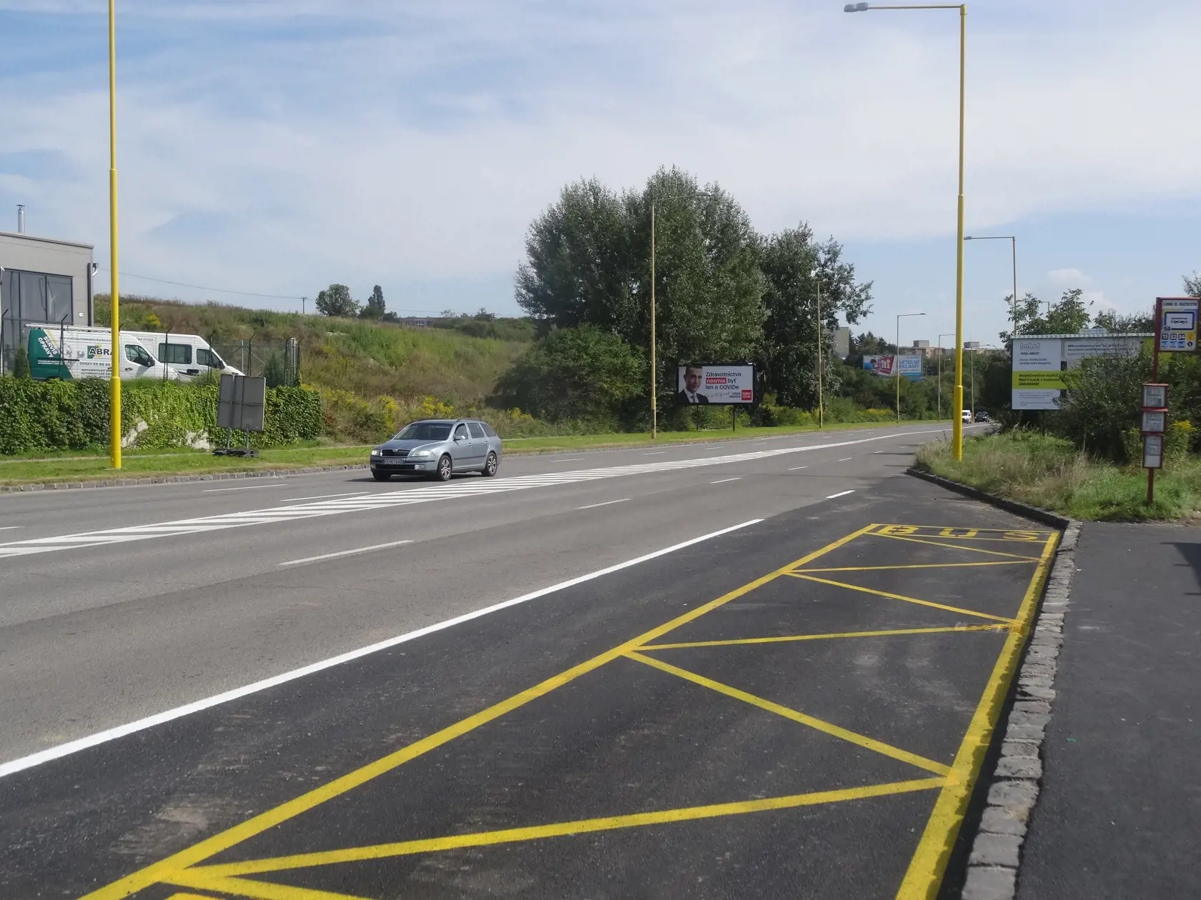 Hlavná cesta, ktorá vedie vedľa rómskeho sídliska. Je zrejmé, že jazdný pruh od sídliska, je čerstvo zrekonštruovaný. Pribudlo aj dopravné značenie na zastávke MHD.