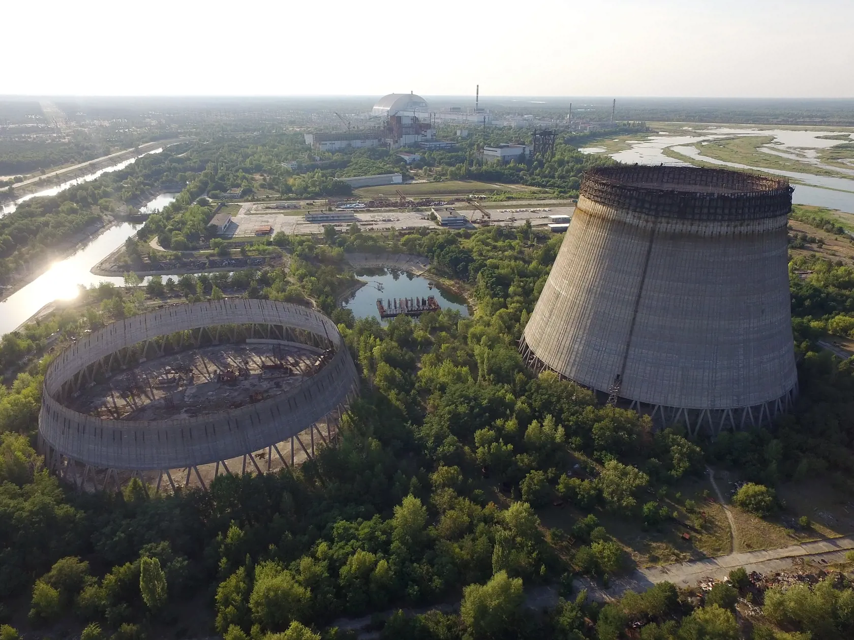 CHORNOBYL, UKRAINE - AUGUST 18:  In this aerial view abandoned, partially-completed cooling towers stand at the Chernobyl nuclear power plant as the new, giant enclosure that covers devastated reactor number four stands behind on August 18, 2017 near Chornobyl, Ukraine. An estimated 900 stray dogs live in the exclusion zone, many of them likely the descendants of dogs left behind following the mass evacuation of residents in the aftermath of the 1986 nuclear disaster at Chernobyl. Volunteers, in