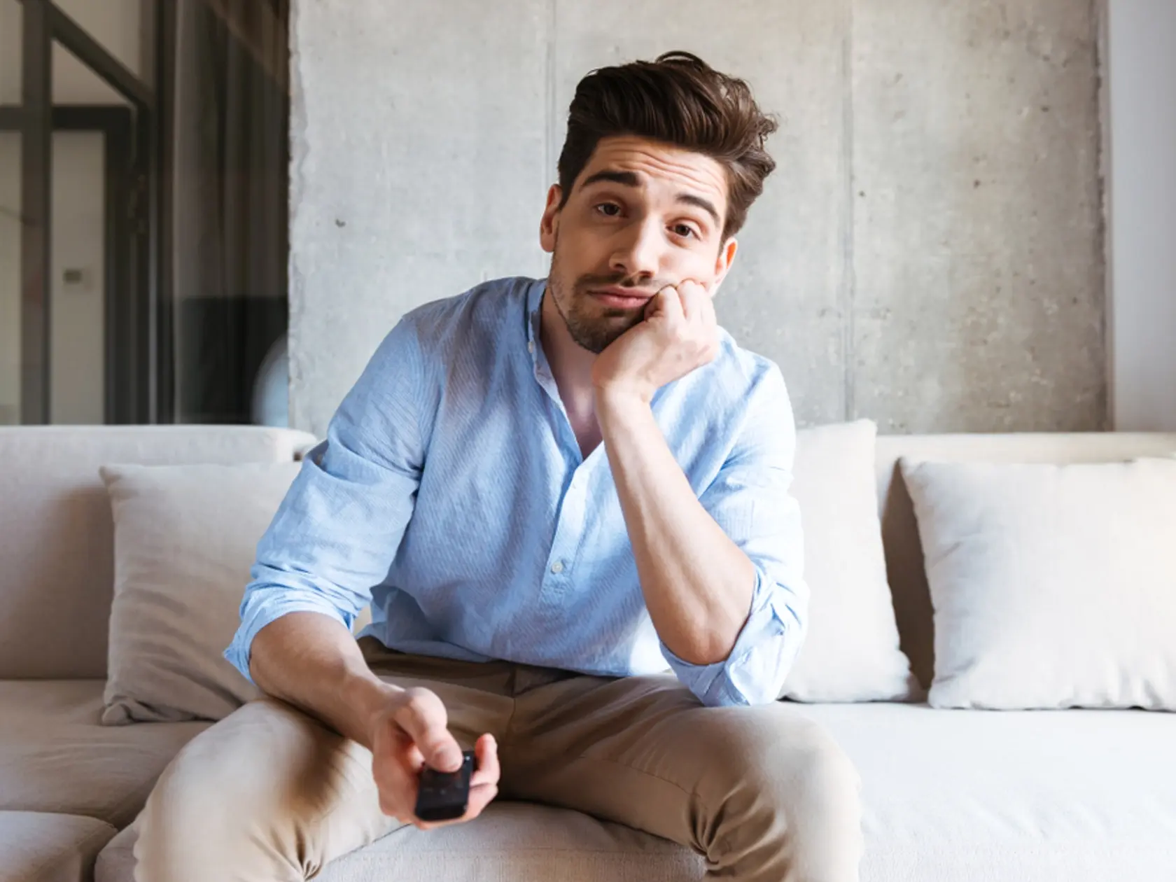 Bored,Young,Man,Holding,Tv,Remote,Control,While,Sitting,On