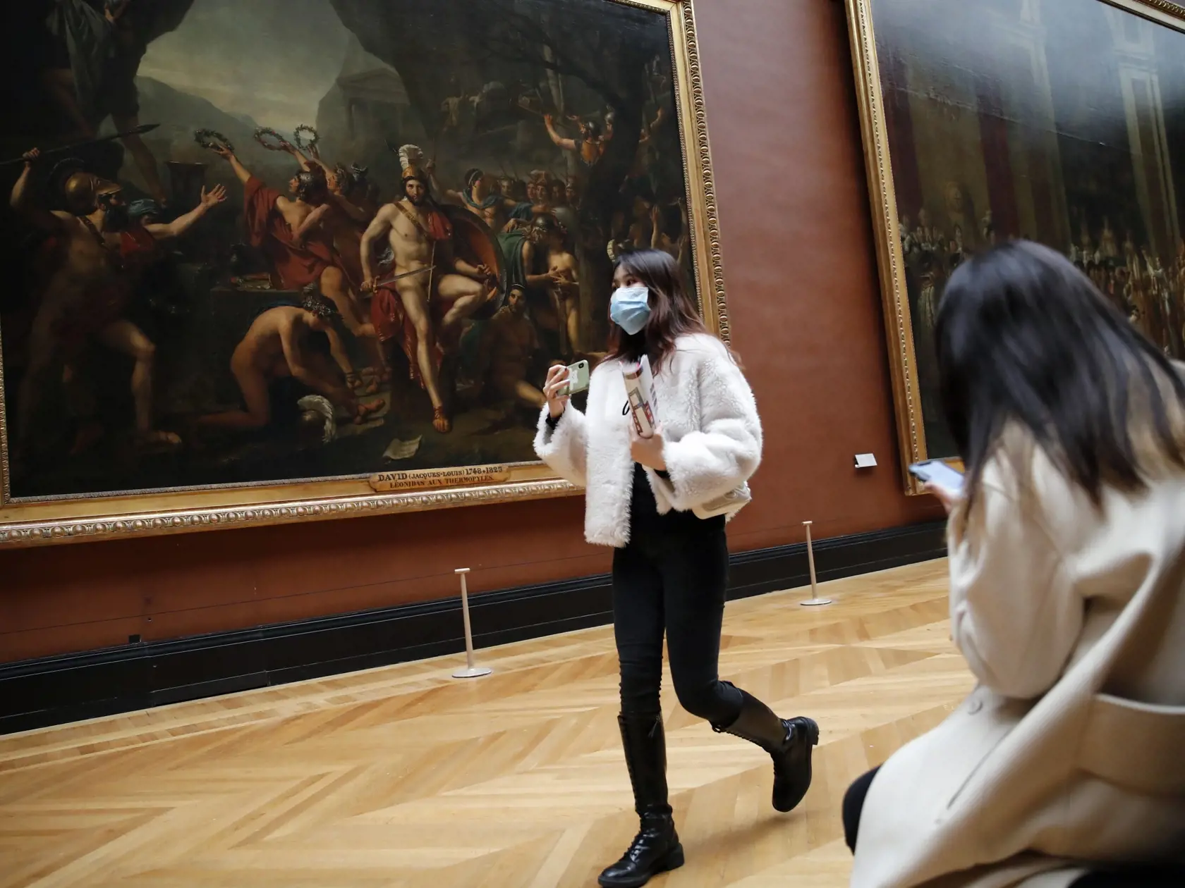 Žena s ochranným rúškom kráča pred olejom na plátne z roku 1814 s názvom Leonidas v Termopylách od Jacques-Louis Davida v múzeu Louvre v Paríži 5. marca 2020.