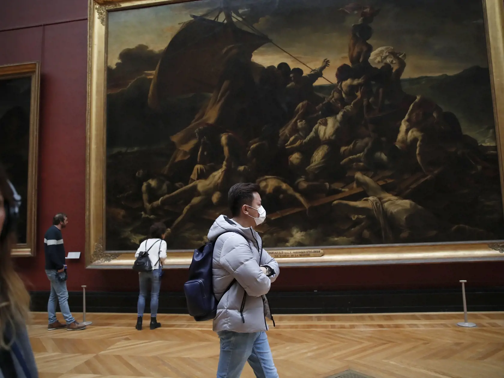 Turista s ochranným rúškom kráča popred obraz plť Medúzy od francúzskeho maliara Theodora Gericaulta v múzeu Louvre v Paríži 5. marca 2020.