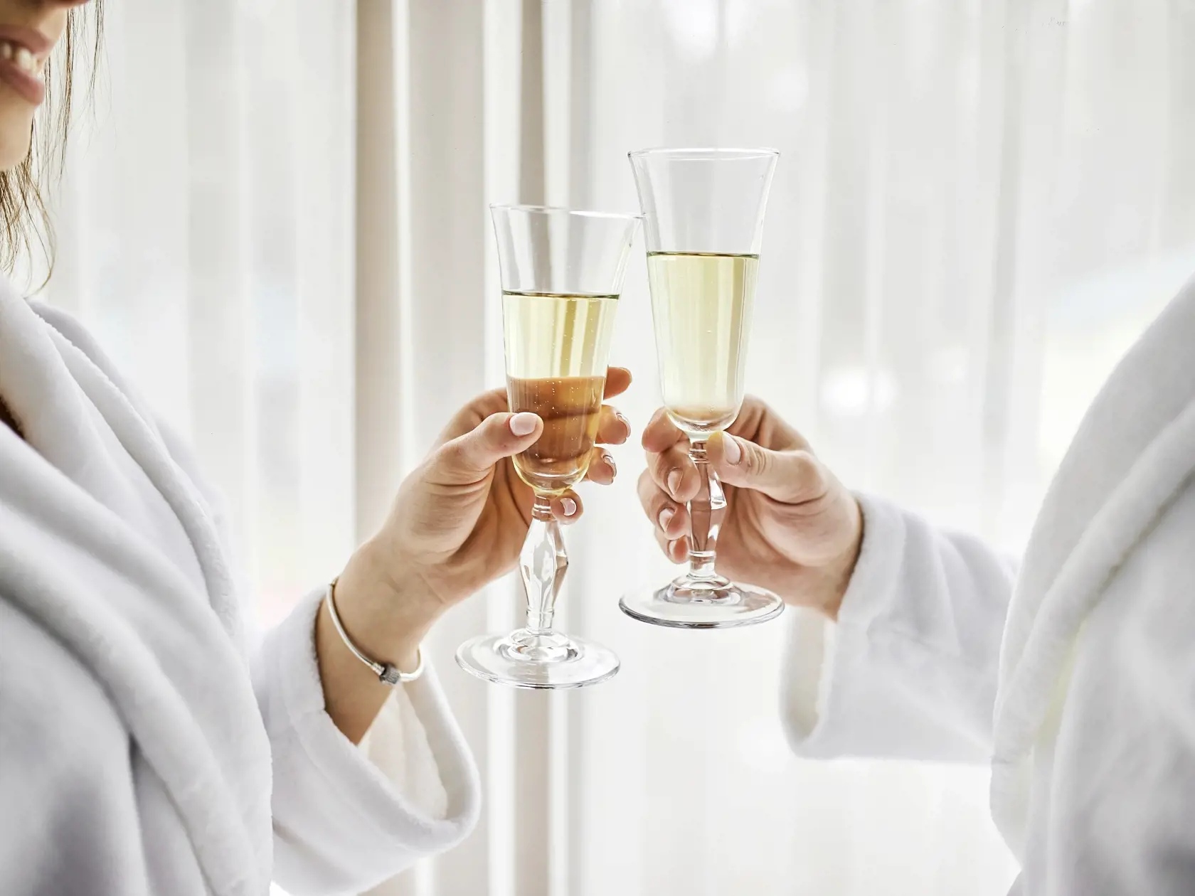 Beauty, spa, healthy lifestyle concept. Beautiful young couple in bathrobes relaxing at luxury hotel room. The boy and the girl are resting in a cozy place and drinking wine. Wellness theme