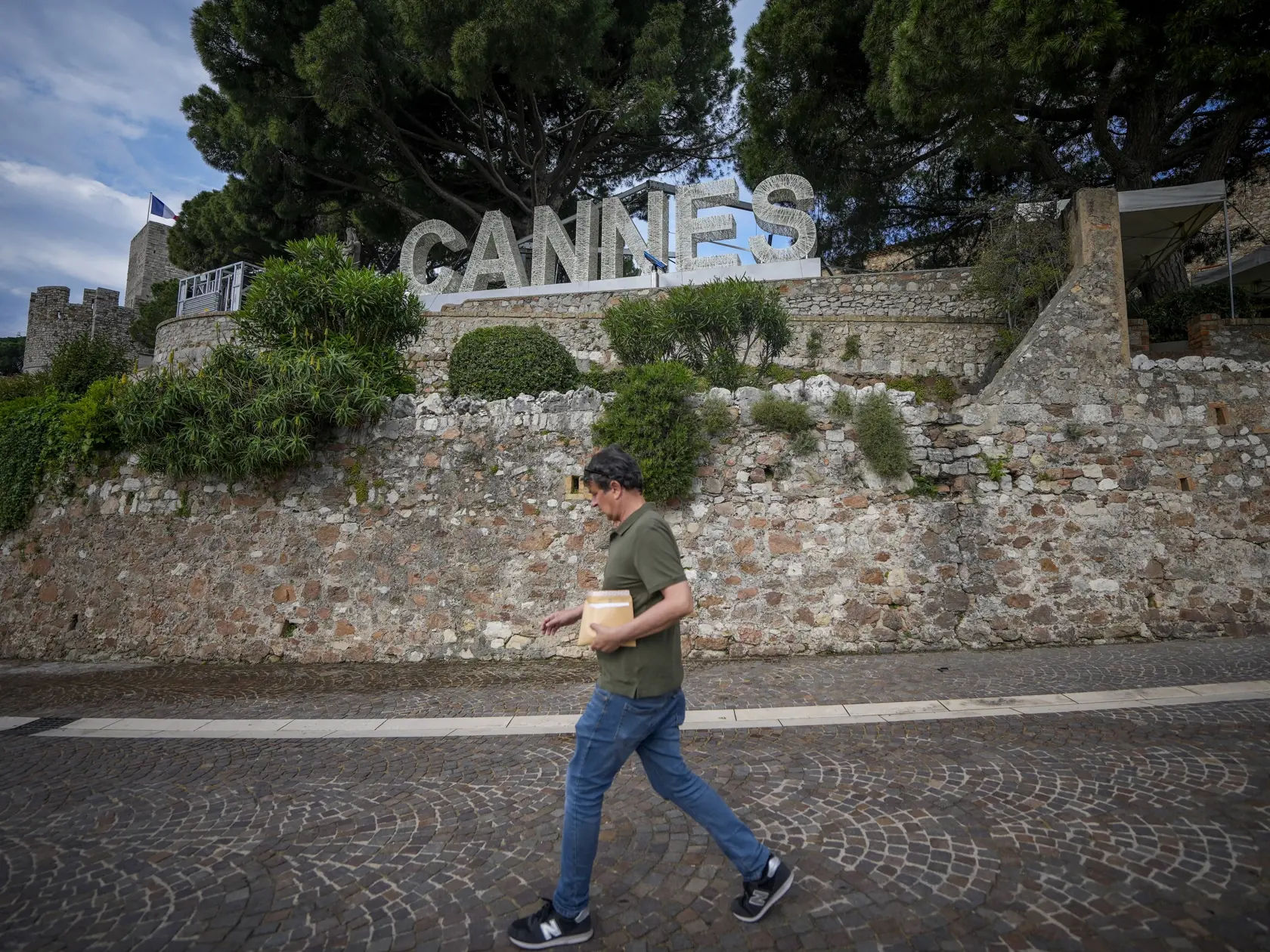 Muž kráča pred nápisom Cannes pred 77. medzinárodným filmovým festivalom v Cannes v južnom Francúzsku v pondelok 13. mája 2024. Filmový festival v Cannes sa začne 14. mája a potrvá do 25. mája 2024.
