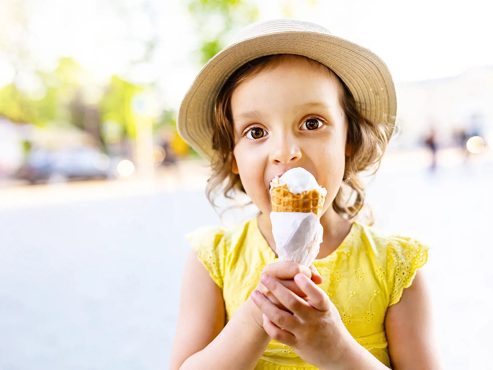 a child eats ice cream in the summer when it's hot outside. Ice cream in a waffle cone. A happy and contented child in a hat and dress.