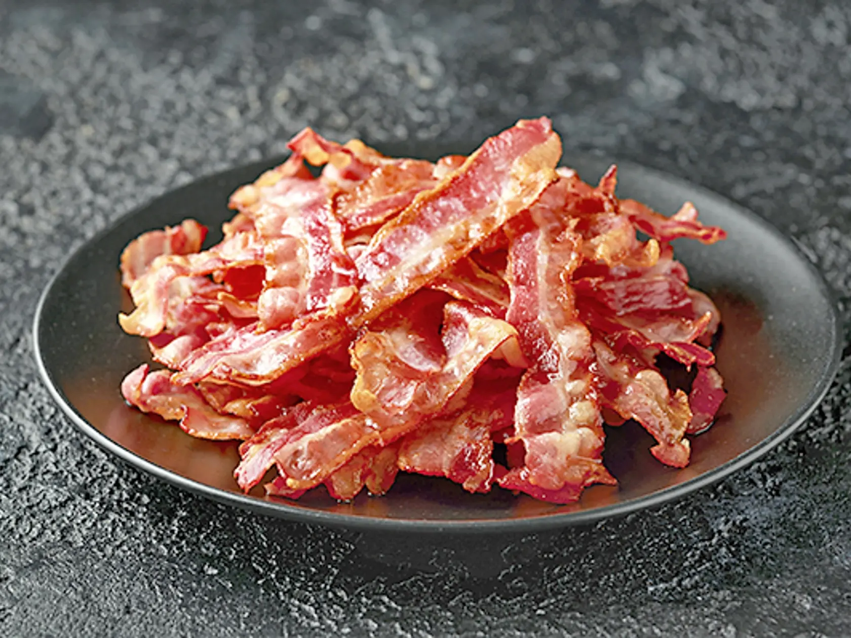 Fried crunchy Streaky Bacon pieces in a black plate