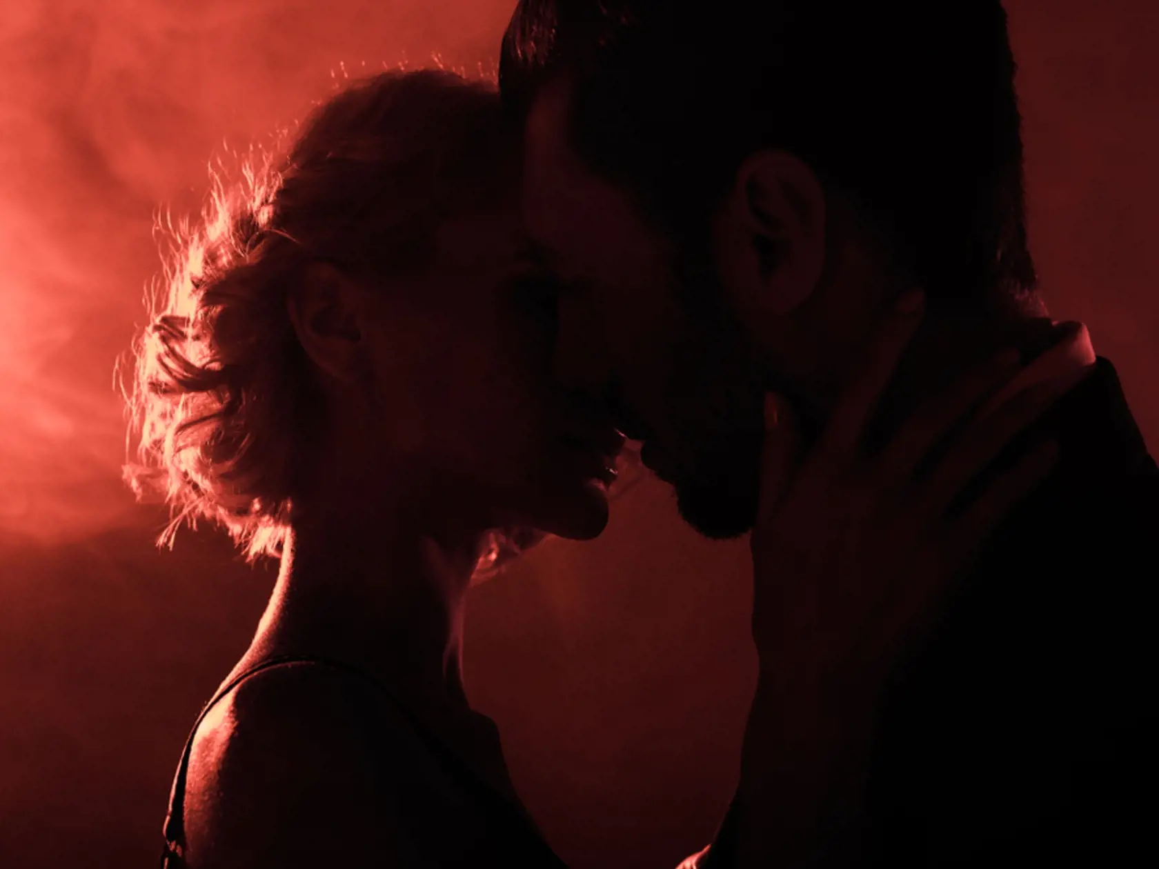 Attractive,Young,Couple,Almost,Kissing,On,Red,Smoke,Background