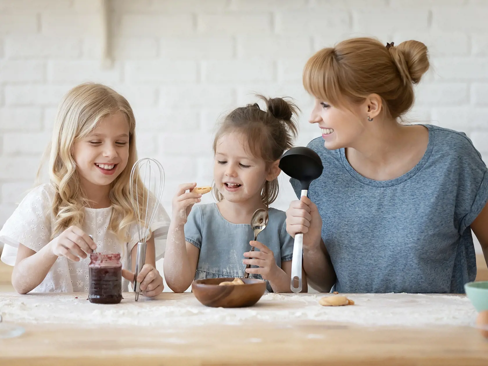 Happy millennial mother and two cute little daughters preparing to taste home baked pastries they cooked together with jam, young mommy and her children willing to enjoy own making fresh home bakery