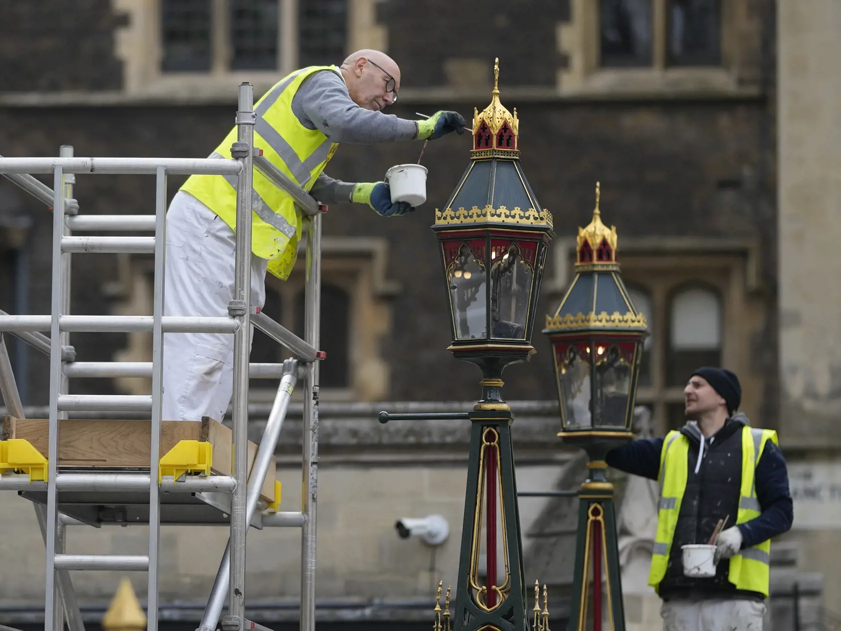 Maliari premaľovávajú lampy pred Westminsterským opátstvom počas príprav na korunováciu britského kráľa Karola III. v Londýne 27. apríla 2023. Korunovácia Karola III. vo Westminsterskom opátstve sa bude konať 6. mája a zúčastnia sa na nej predstavitelia mnohých krajín sveta.