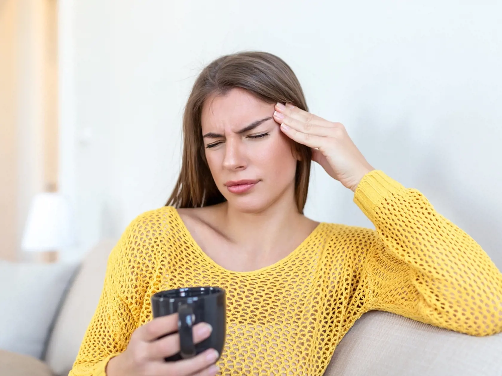 Depressed,Young,Woman,Having,Headache,While,Drinking,Coffee,On,Sofa