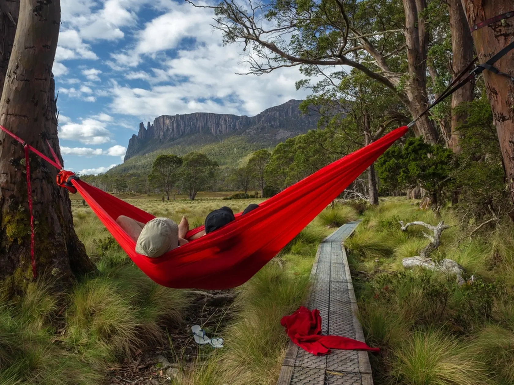 A pair of traveller couple relaxing on a hammock and watching  the peak of Mount Oakleigh in the Overland Track, Cradle Mountain - Lake St Clair National Park, Tasmania, Australia