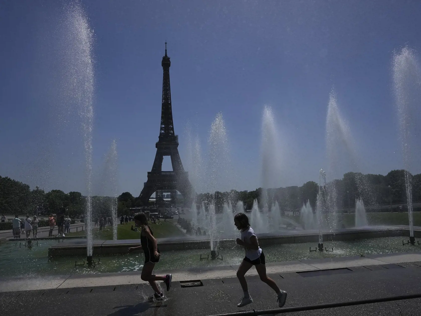 Ľudia bežia okolo fontány pri Eiffelovej veži v Paríži počas horúčav.