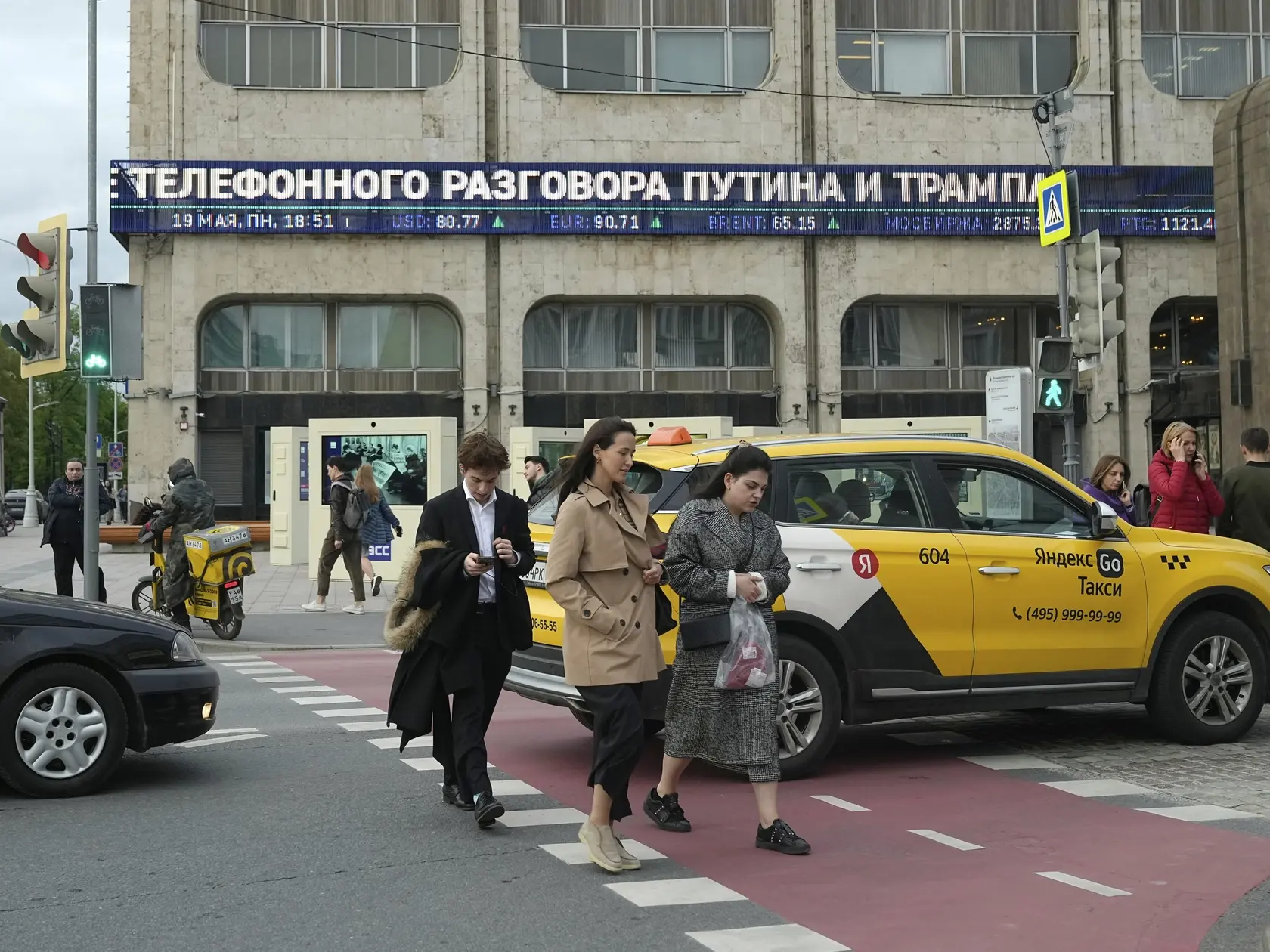 Ľudia kráčajú cez cestu v Moskve, v pozadí ticker informuje o telefonátom medzi americkým prezidentom Donaldom Trumpom a ruským prezidentom Vladimirom Putinom v pondelok 19. mája 2025. Telefonát trval viac než dve hodiny. Šéf Kremľa ho označil za úprimný, informatívny a užitočný. Rusko je podľa Putinových slov pripravené spolupracovať s Ukrajinou na memorande o budúcich mierových rokovaniach, ktoré by tiež mohlo zahŕňať otázky budúceho prímeria a zásady urovnania konfliktu. FOTO TASR/AP