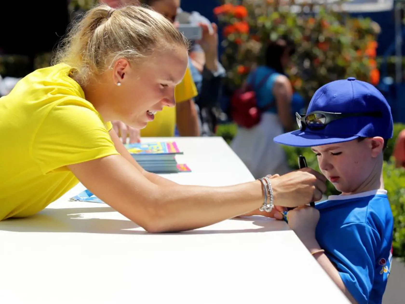 In this photo released by Tennis Australia, Denmark's Caroline Wozniacki signs her autograph onto the shirt of a young fan at the Australian Open tennis championship in Melbourne, Australia, Monday, Jan. 13, 2014. (AP Photo/Tennis Australia,Fiona Hamilton)