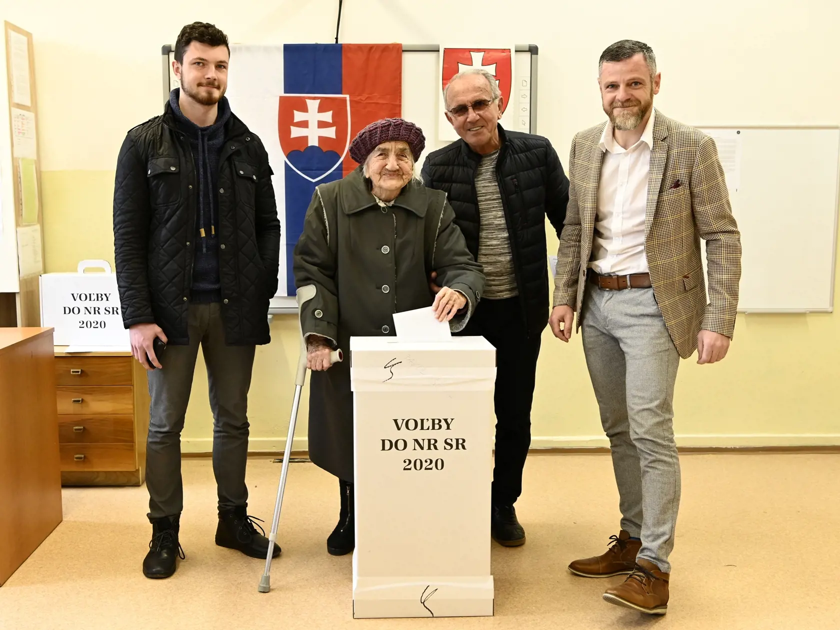 Na snímke druhá zľava 103-ročná volička Gizela Dvončová  spolu s 21-ročným pravnukom Michalom (vľavo), 43-ročným vnukom Jurajom (vpravo) a 75- ročným synom Ľubomírom vhadzuje hlasovací lístok v obálke do volebnej urny vo voľbách do Národnej rady SR v Partizánskom 29. februára 2020. FOTO TASR - Radovan Stoklasa