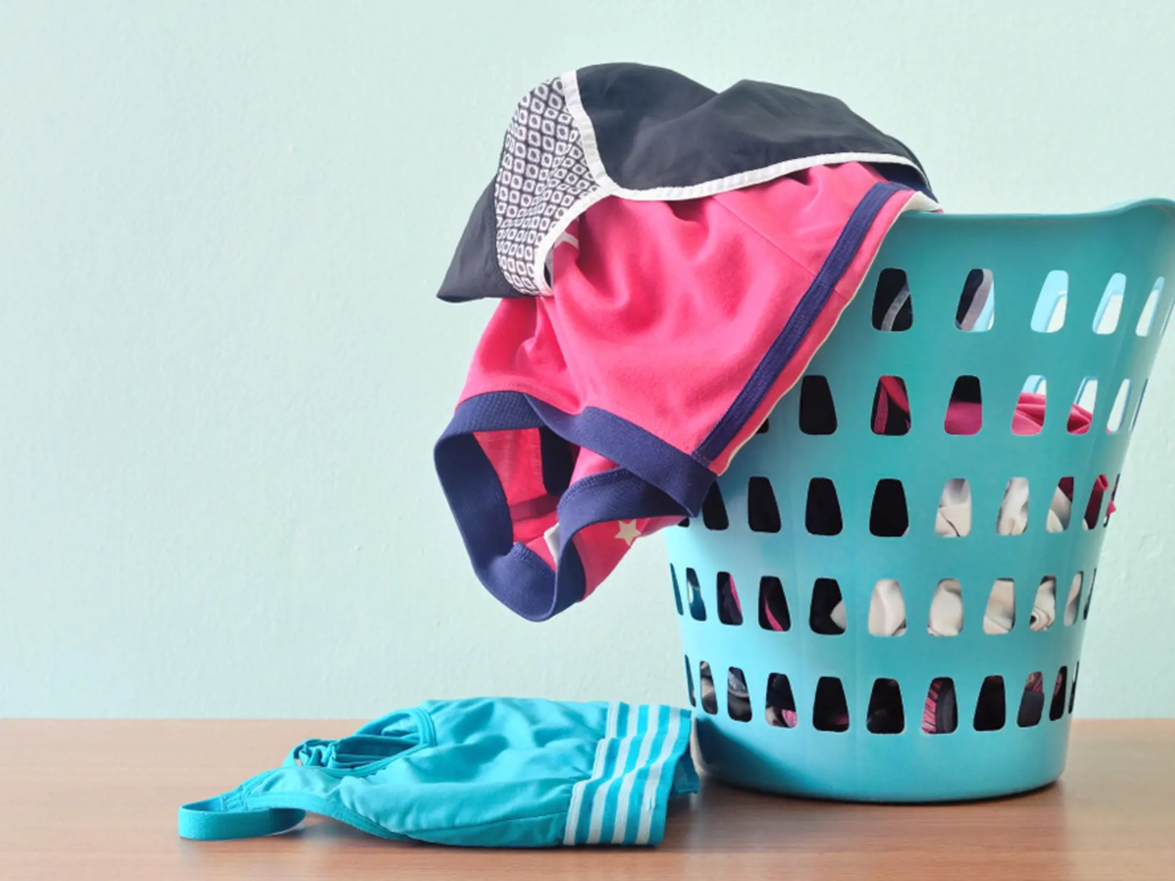 Piles of sport cloths in laundry basket in blue background. Messy, cluttered most active teenager room.
