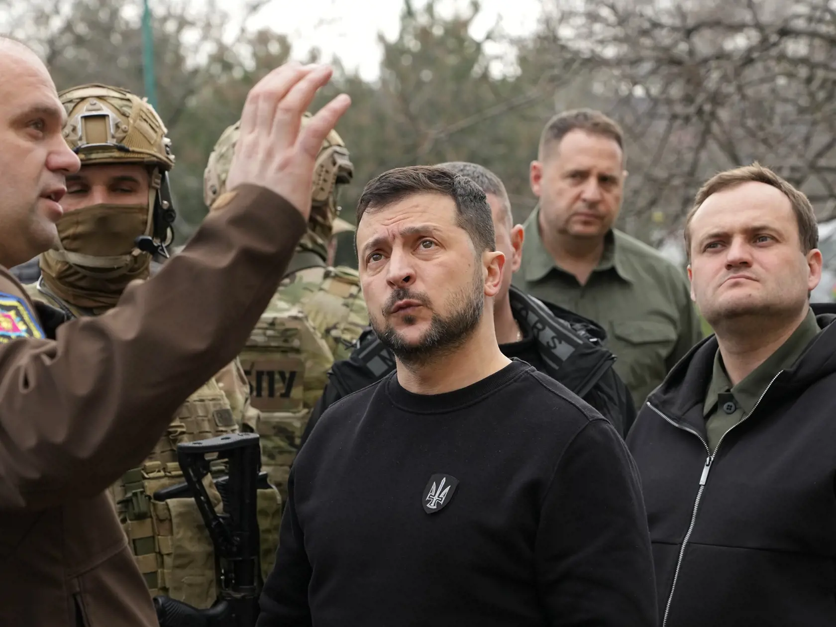 Ukrajinský prezident Volodymyr Zelenskyj (uprostred) počúva, keď si prezerá  obytné budovy poškodené po raketových útokoch v ukrajinskom meste Záporožie v pondelok 27. marca 2023.