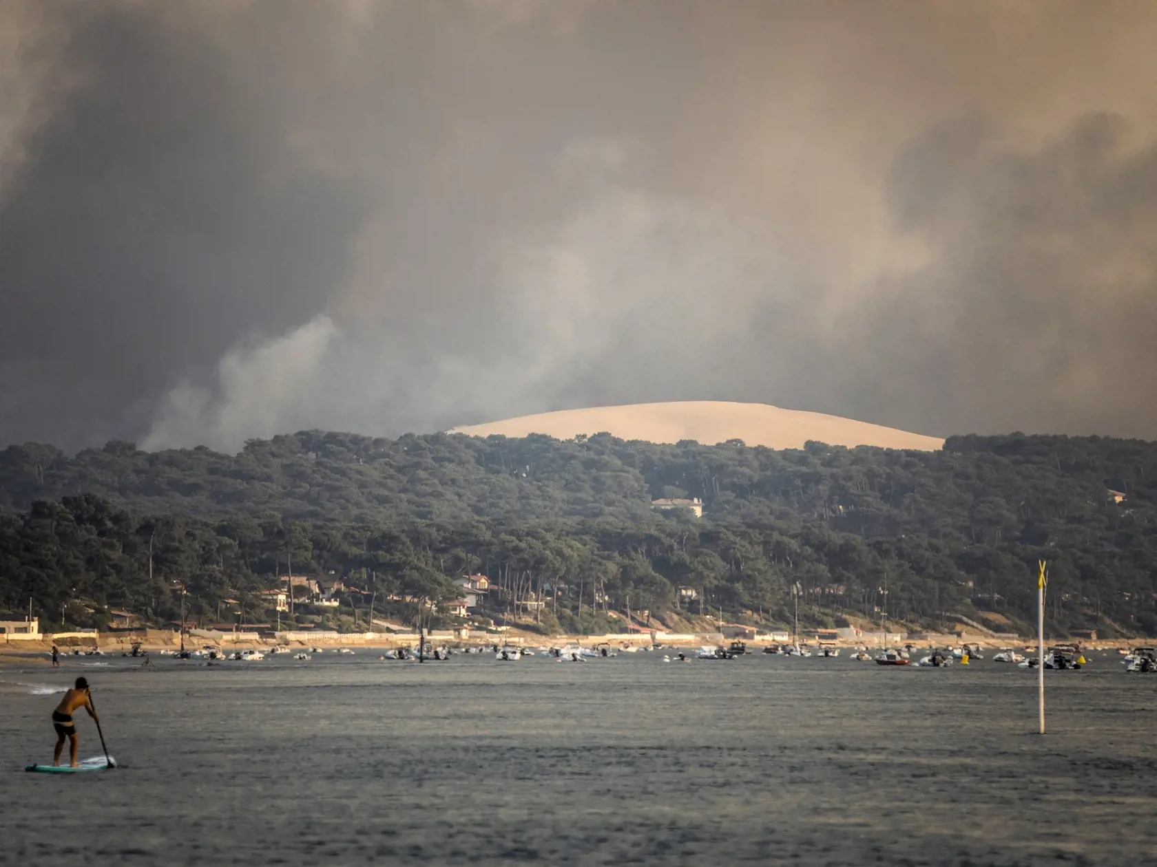 KK36 Pilat sur Mer - Dym stúpa nad plážou Pilat sur Mer v juhozápadnom Francúzsku z obrovského lesného požiaru, ktorý zachvátil tisícročný les  18. júla 2022.