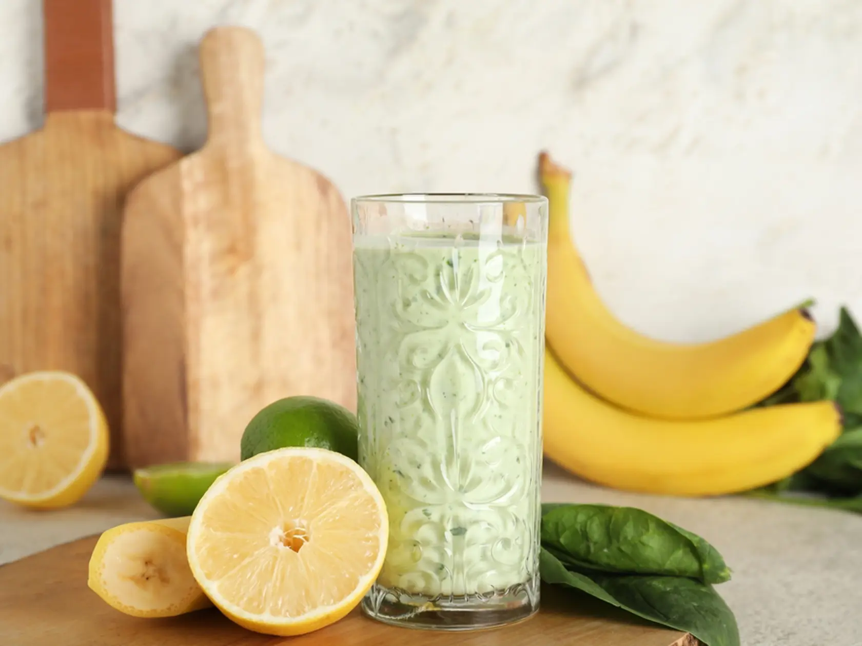 Glass of fresh spinach smoothie with lemon and banana on white background