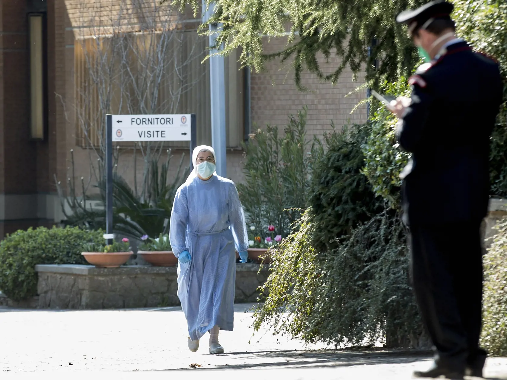 MIK 34 Grottaferrata - Mníška s ochranným rúškom a s rukavicami kráča ku karabinierovi (policajtovi) pred kláštorom Istituto Figlie di San Camillo v Grottaferrata, neďaleko Ríma, v Taliansku 20. marca 2020. Infekcia koronavírusom postihla v Ríme dva kláštory. Rímsky denník Il Messaggero v piatok citoval hlavného komisára pre zdravie v regióne Lazio a uviedol, že 59 mníšok v Istituto Figlie di San Camillo v horskom mestečku Grottaferrata malo pozitívny test na COVID-19.

A nun wearing a mask and 