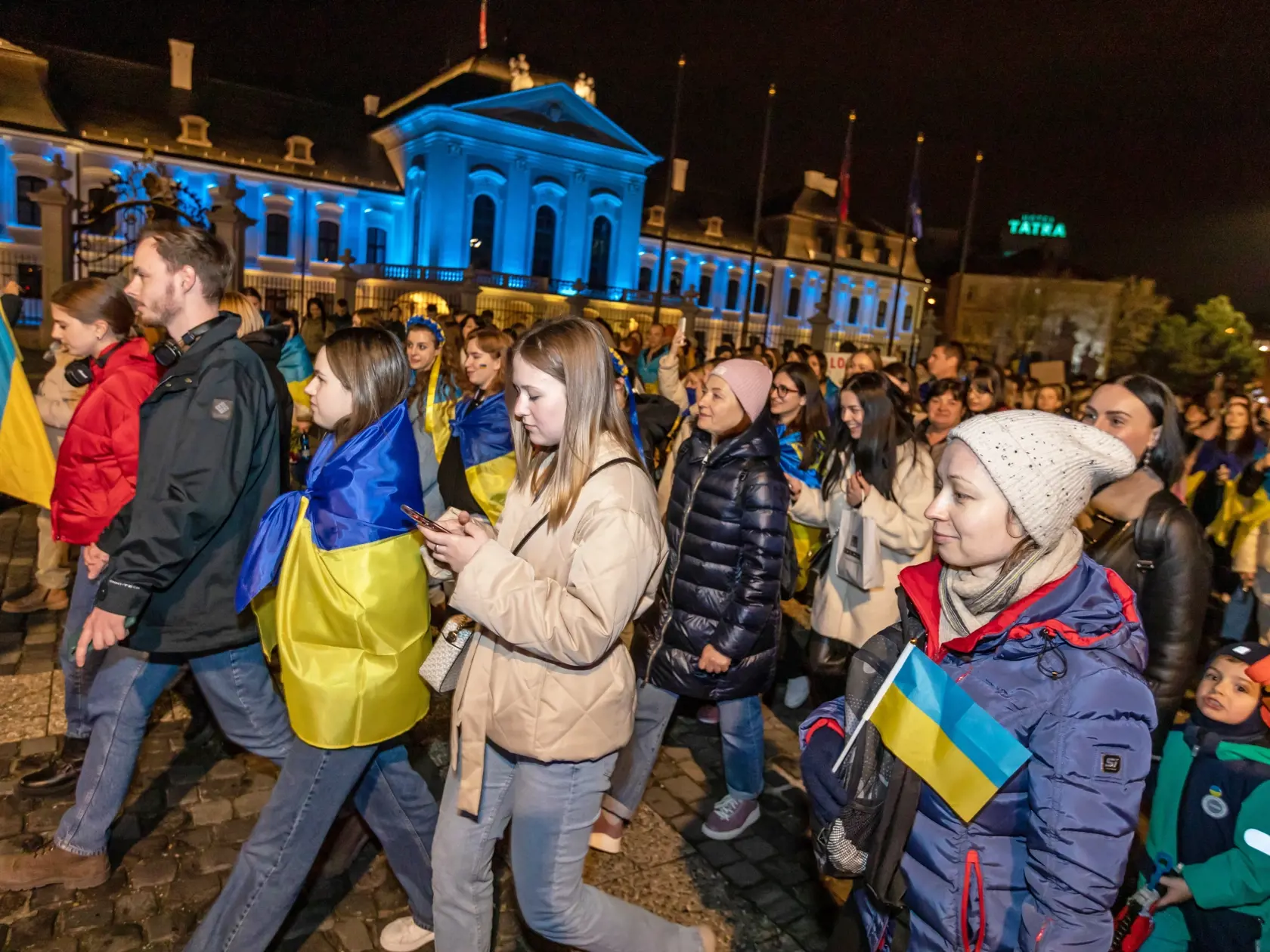 Na snímke sú ľudia pred Kanceláriou prezidenta, ktorá bola symbolicky nasvietená v ukrajinsko modro-žltej farbe. Stalo sa tak v deň výročia vpádu ruských vojsk na Ukrajinu.