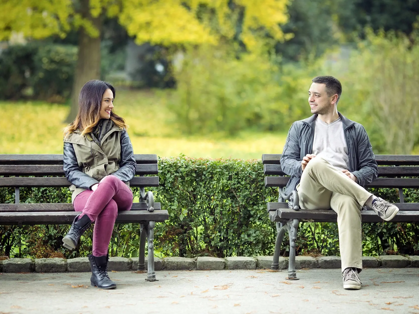 Two young people sitting on benches in a park and talking