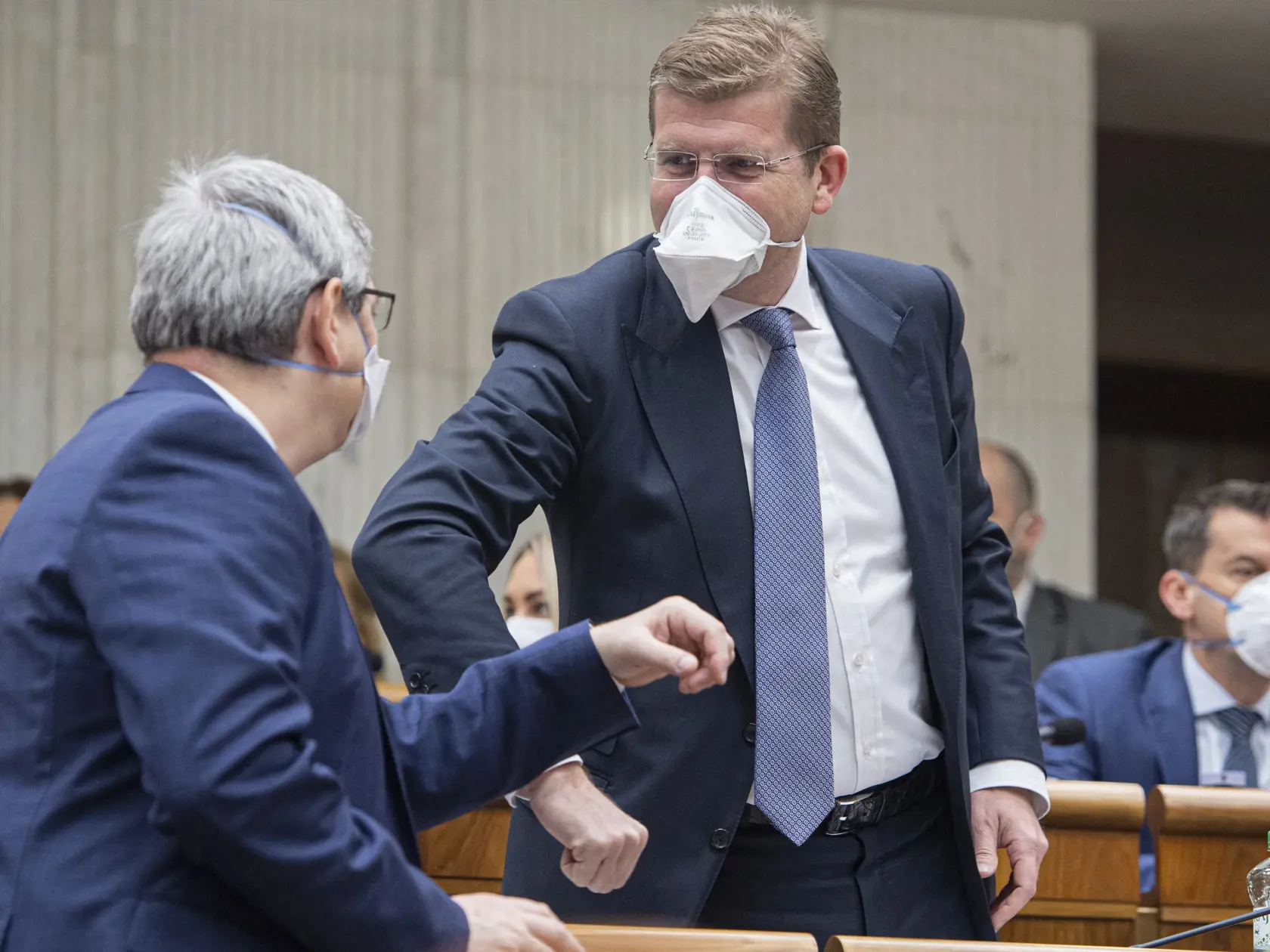 Opozičný poslanec Peter Žiga (SMER-SD, vpravo) s ochranným rúškom na tvári sa zdraví lakťom so svojím kolegom počas druhej schôdze Národnej rady Slovenskej republiky. Bratislava, 24. marca 2020.  FOTO TASR - Michal Svítok