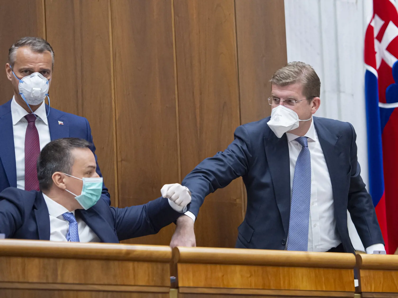 Opoziční poslanci Peter Žiga (vpravo), Richard Raši (uprostred) a Erik Tomáš (všetci SMER-SD) s ochrannými rúškami na tvári sa zdravia lakťom počas druhej schôdze Národnej rady Slovenskej republiky. Bratislava, 24. marca 2020.  FOTO TASR - Michal Svítok