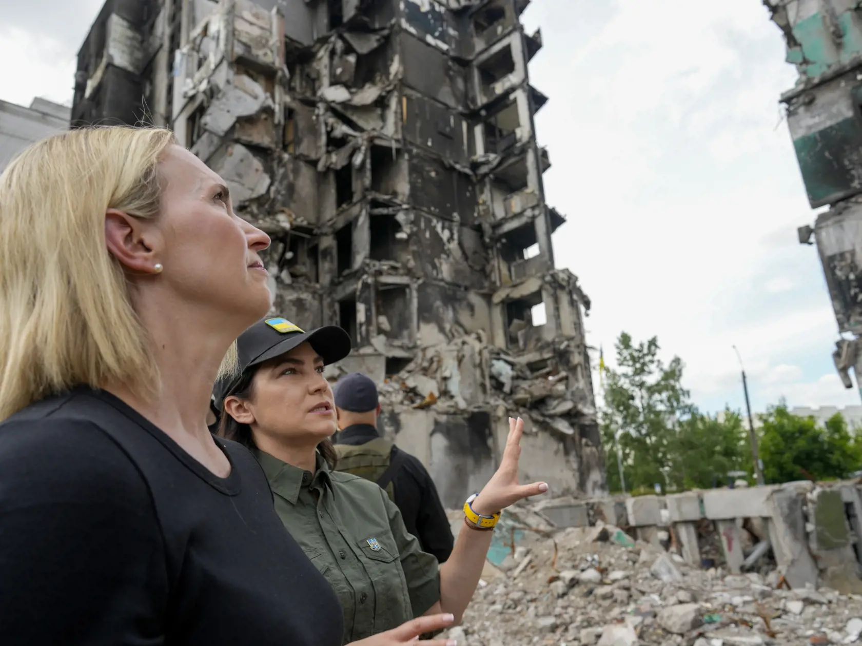 Generálna prokurátorka Ukrajiny  Iryna Venediktovová (uprostred vpravo) a americká veľvyslankyňa na Ukrajine Bridget Brinková (uprostred) sa pozerajú na zničenú obytnú budovu počas útokov v Borodjanke na predmestí Kyjeva 4. júna 2022. 
U.S. ambassador to Ukraine Bridget Brink, left, listens to Ukraine's Prosecutor General Iryna Venediktov during a tour of a d