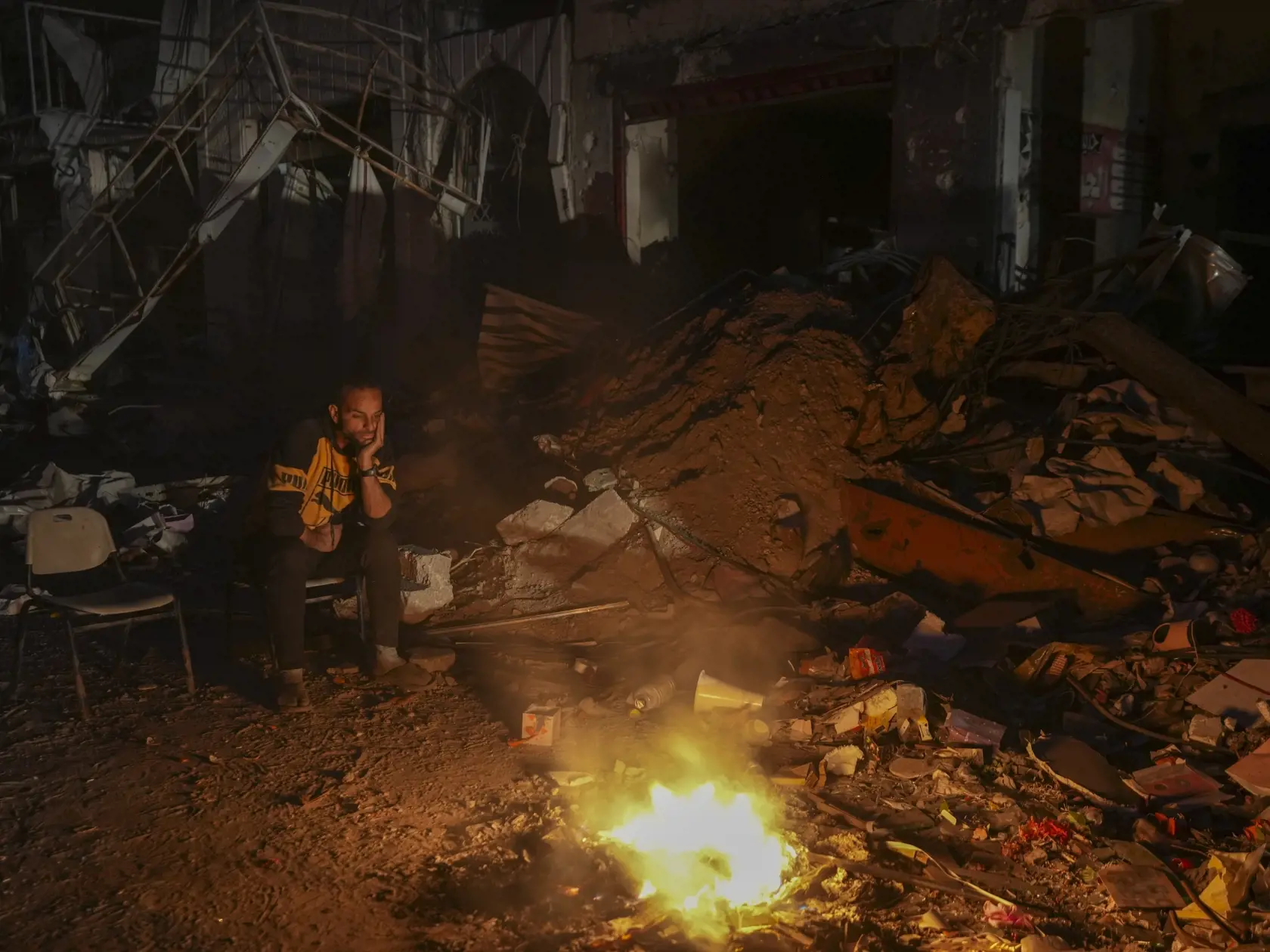 Na snímke muž sedí pri ohni medzi troskami a zničenými budovami počas bojov medzi izraelskom armádou a palestínskym militantným hnutím Hamas v meste Gaza v utorok 4. februára 2025.