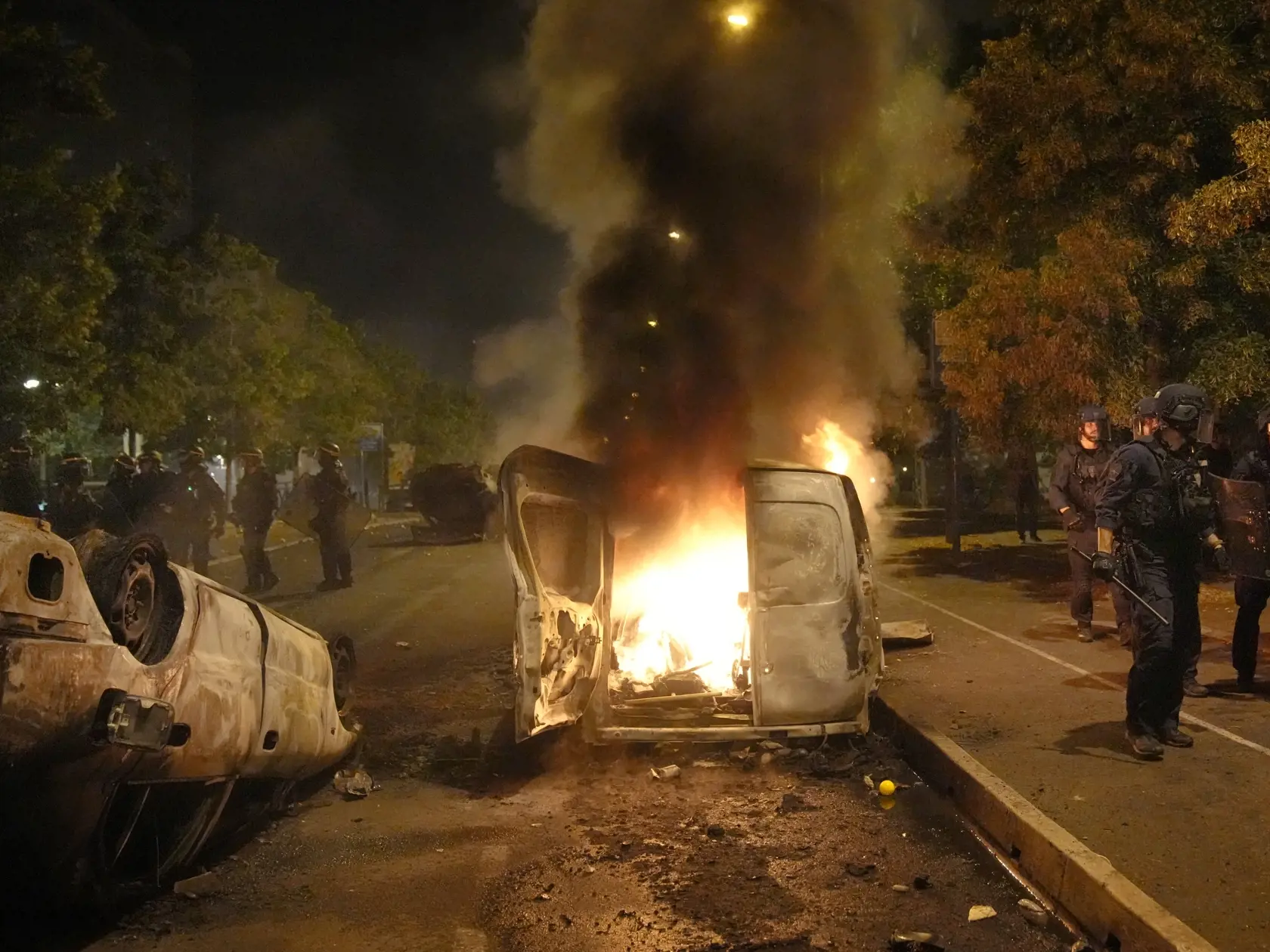 Policajti kráčajú okolo horiacich áut v meste Nanterre na predmestí Paríža 29. júna 2023. Násilné protesty otriasli v noci na štvrtok mestečkami na predmestí Paríža po tom, čo polícia zastrelila počas dopravnej kontroly tínedžera a klamala o okolnostiach jeho úmrtia. TASR o tom informuje podľa správy agentúry AFP. Polícia zastavila pre dopravný priestupok v utorok večer 17-ročného mladíka, ktorého úrady identifikovali len ako Naela M.