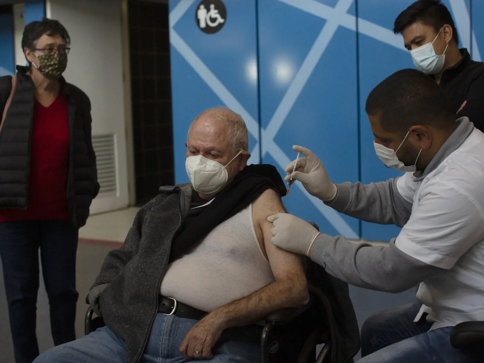 KK33 Jeruzalem - Na snímke muž počas očkovania vakcínou proti ochoreniu Covid-19 od spoločnosti Pfizer vo vakcinačnom centre 14. januára 2021 v Jeruzaleme. FOTO TASR/AP
A medical professional administers the Pfizer COVID-19 vaccine to a man under the watchful eyes of his wife and home health care aide, who also got the vaccine, at a makeshift vaccination center in a sports arena in Jerusalem, Thursday, Jan. 14, 2021 . (AP Photo/Maya Alleruzzo)