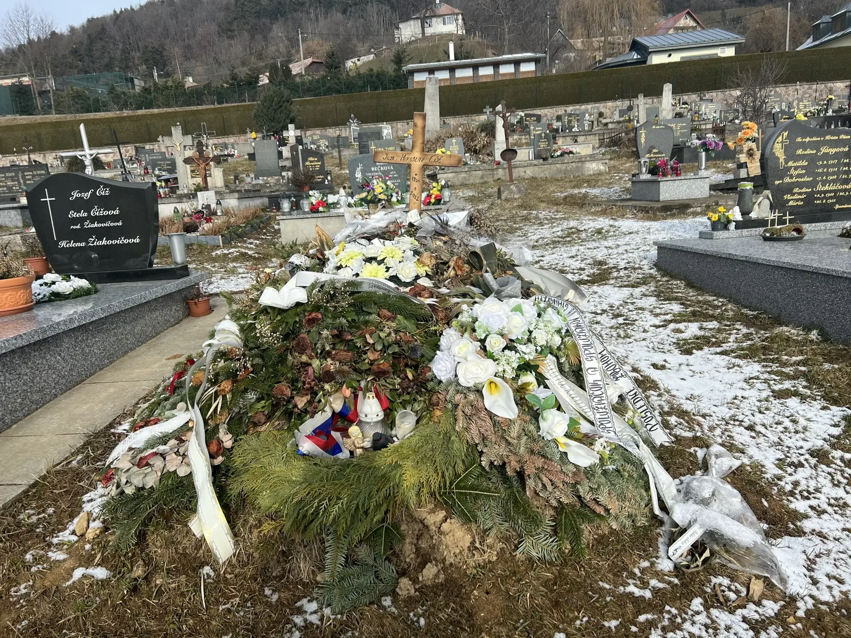 Namiesto pomníka tu dočasne stojí len jednoduchý drevený kríž a hrob pôsobí ako keby sa oň nik nestaral - ležia na ňom staré kvety ešte od pohrebu.
