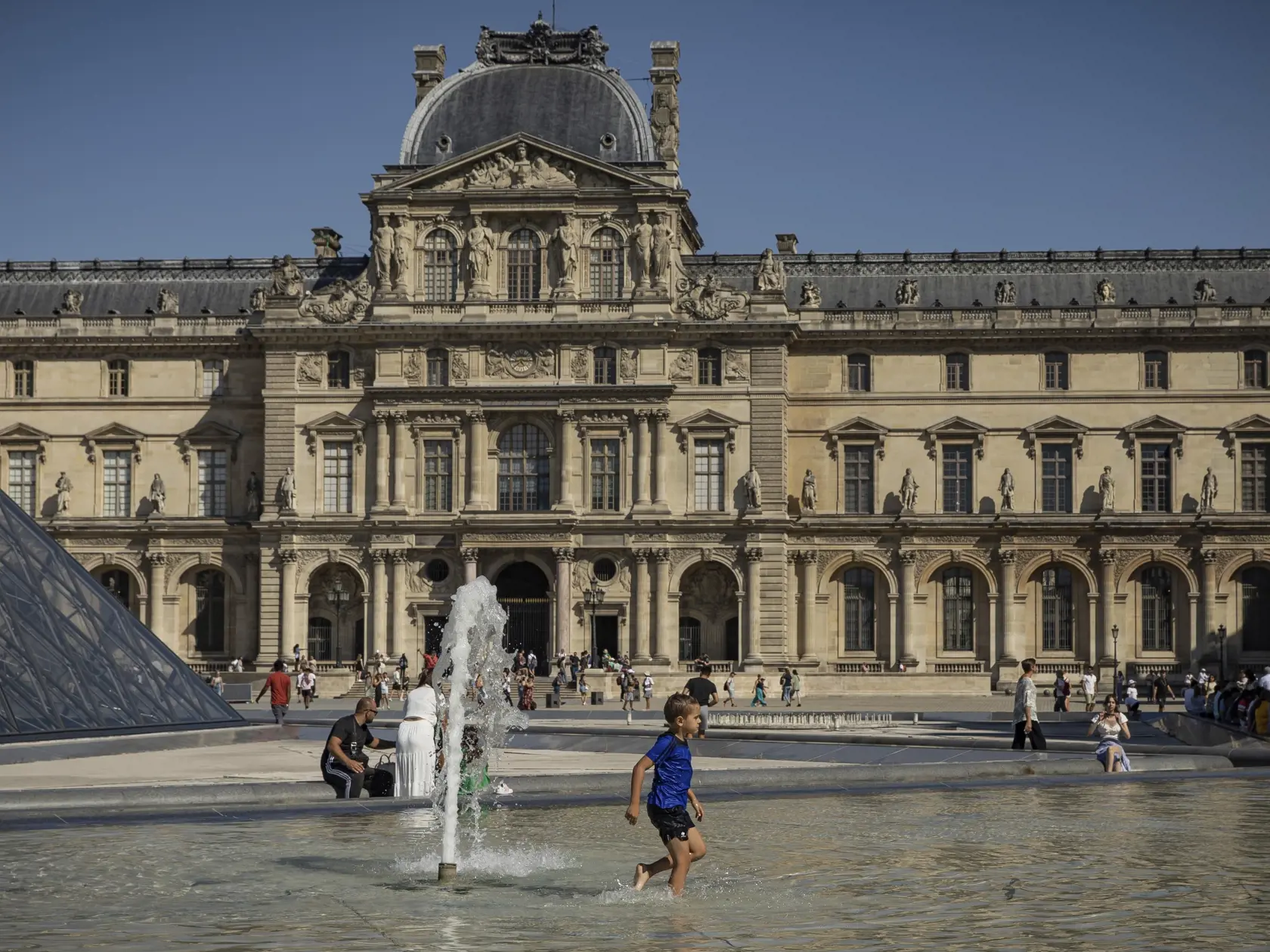 Dieťa sa osviežuje vo fontáne pred múzeom Louvre v Paríži 11. augusta 2022.