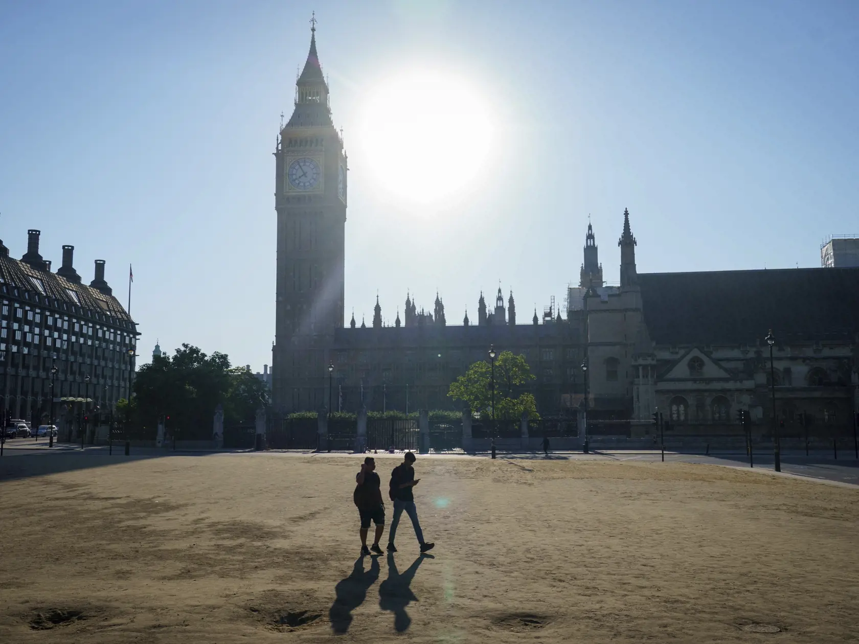 Dvaja ľudia sa prechádzajú po vyschnutej tráve na Parlamentnom námestí  vo Westminsteri počas teplého počasia v Londýne 13. augusta 2022.