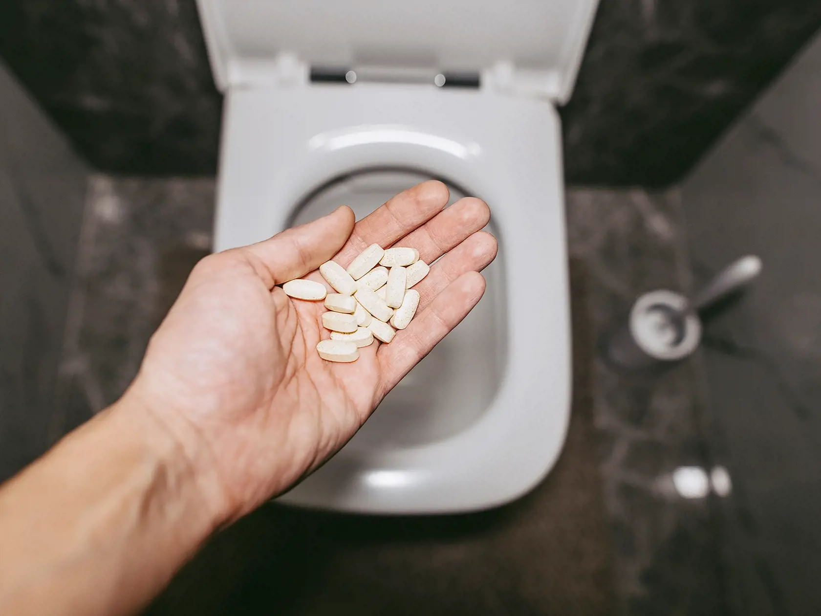 A hand throws pills into the toilet for flushing water