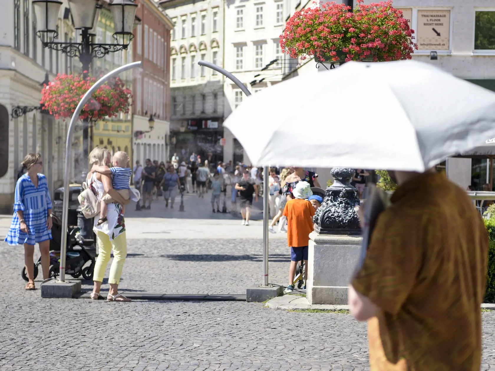 Na snímke vpravo muž s dáždnikom, v pozadí ľudia sa osviežujú pri stojane s vodnou hmlou počas horúceho letného dňa 14. júla 2022 v Bratislave. FOTO TASR - Pavol Zachar