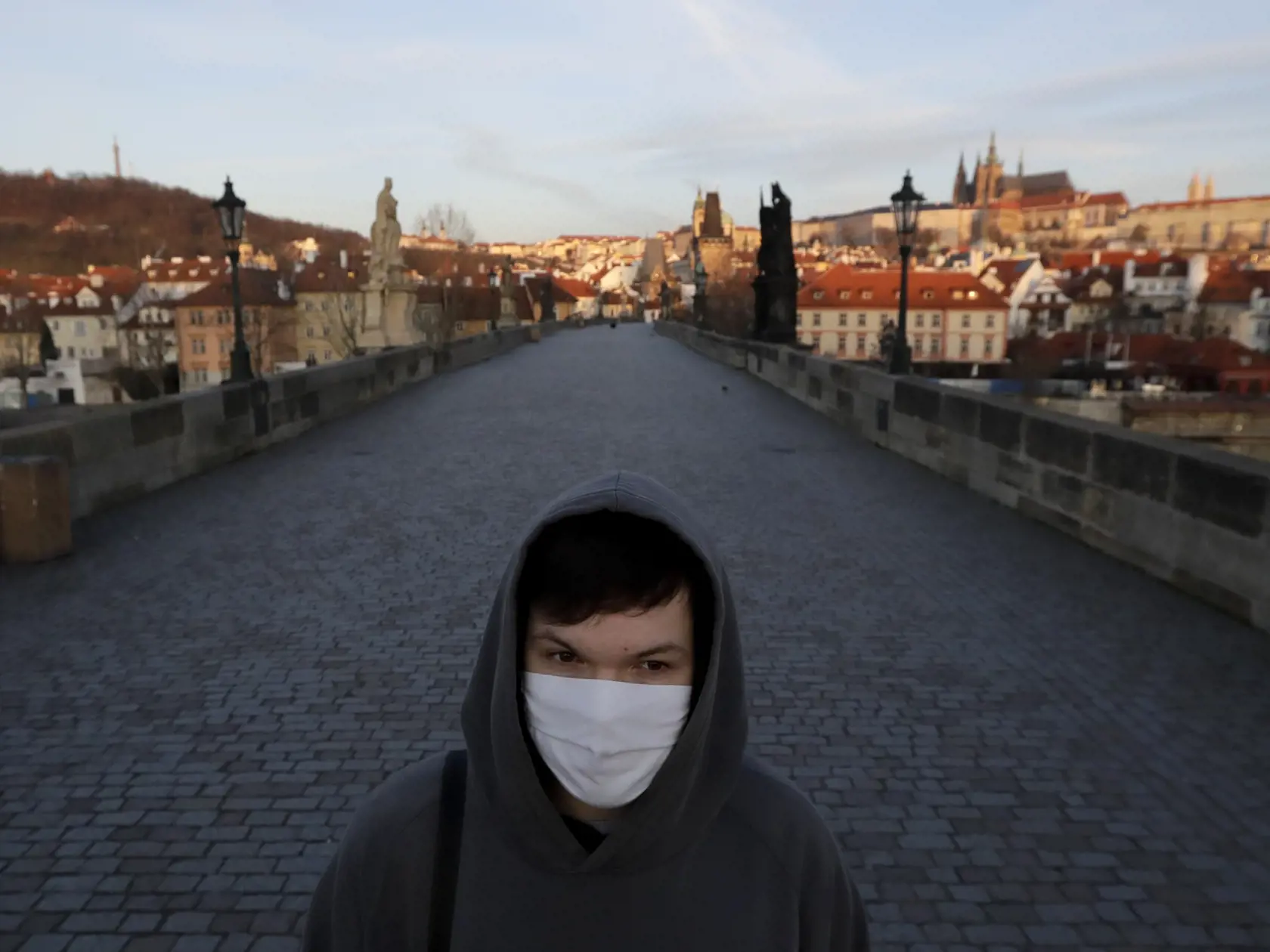 Mladý muž s ochranným rúškom na tvári kráča po Karlovom moste.