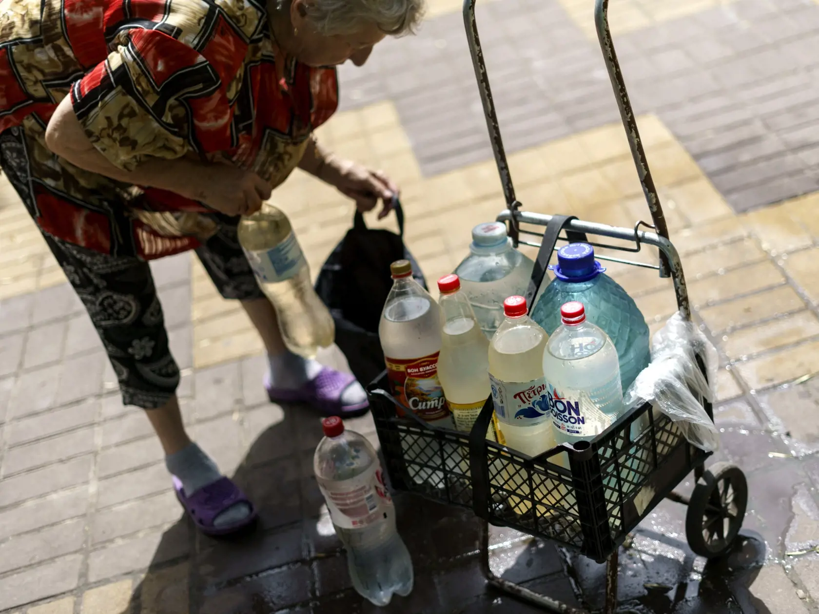 WA 17 Sloviansk - Sedemdesiatšesťročná Ľubov Mahlijová si dáva do tašky zvyšné fľaše, ktoré si naplnila vodou z verejnej studne v meste Sloviansk v Doneckej oblasti na východe Ukrajiny počas 164. dňa ruskej invázie na Ukrajine v sobotu 6. augusta 2022. "Aj keď počujeme sirény a bombardovanie, stále nosíme vodu," povedala. "Je to pre nás veľké riziko, ale čo môžeme robiť?", dodala. Boje medzi ukrajinskými a ruskými silami v blízkosti kľúčového mesta Sloviansk poškodili dôležitú infraštruktúru. Vo