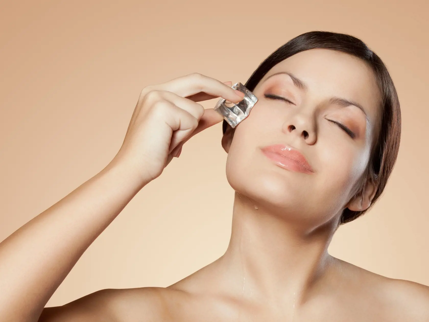 brunette woman holding ice cube on her face