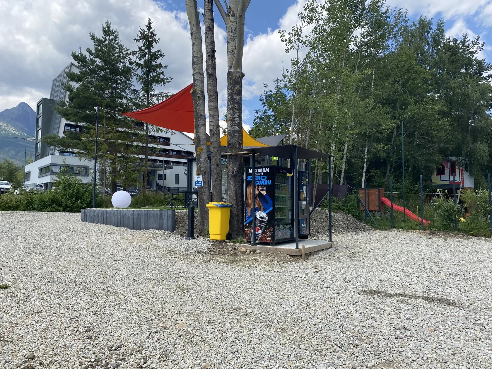 Vedľa múzea sú umiestnené na pozemku vysypanom štrku dva predajné automaty na nápoje.