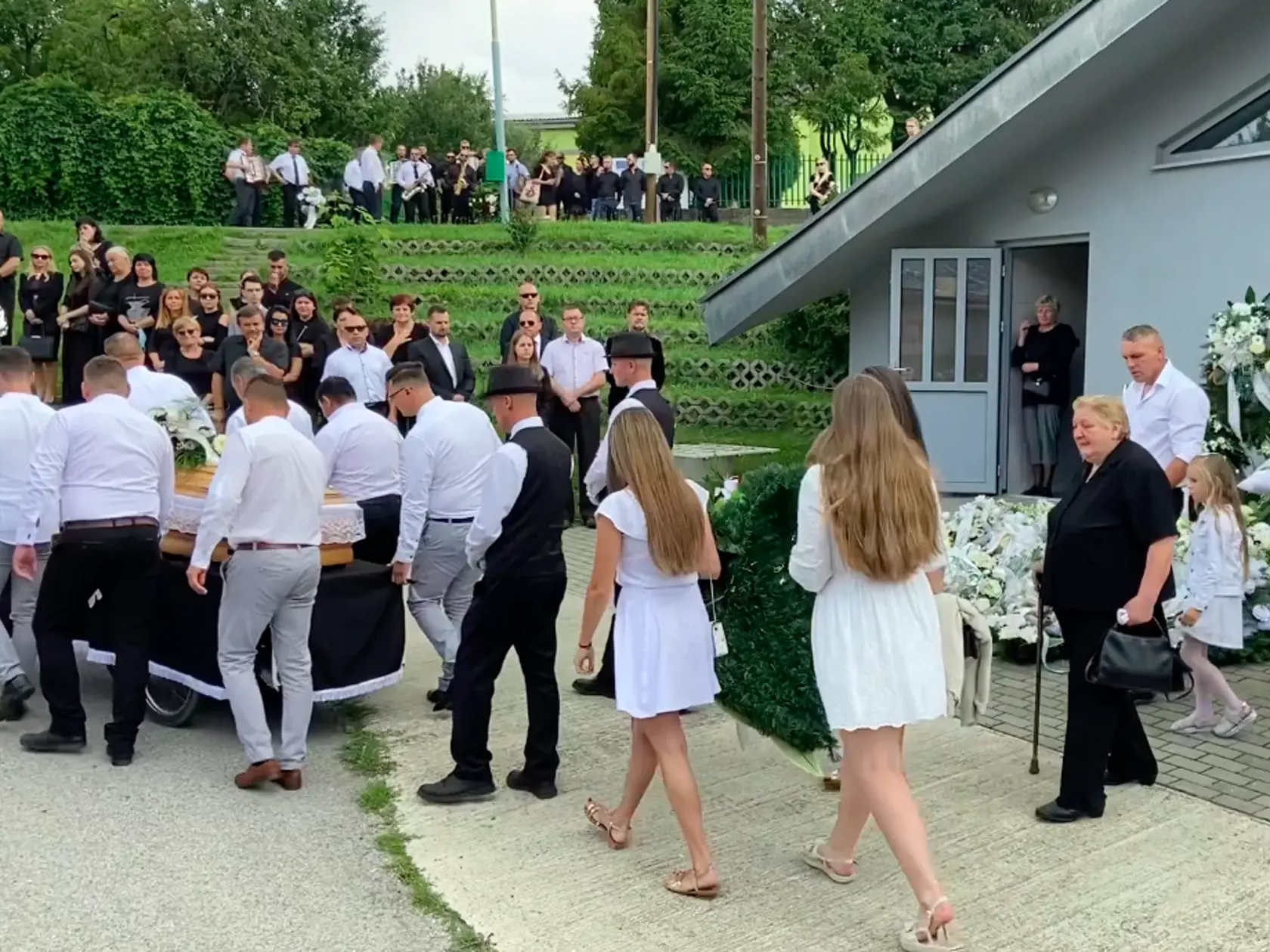 Truhlu s domu smútku vyniesli jeho spoluhráči, za nimi kráčali členky Dievčenského tria, ktoré s kapelou od roku 2018 hrávali. Niesli veľké kvetinové srdce.