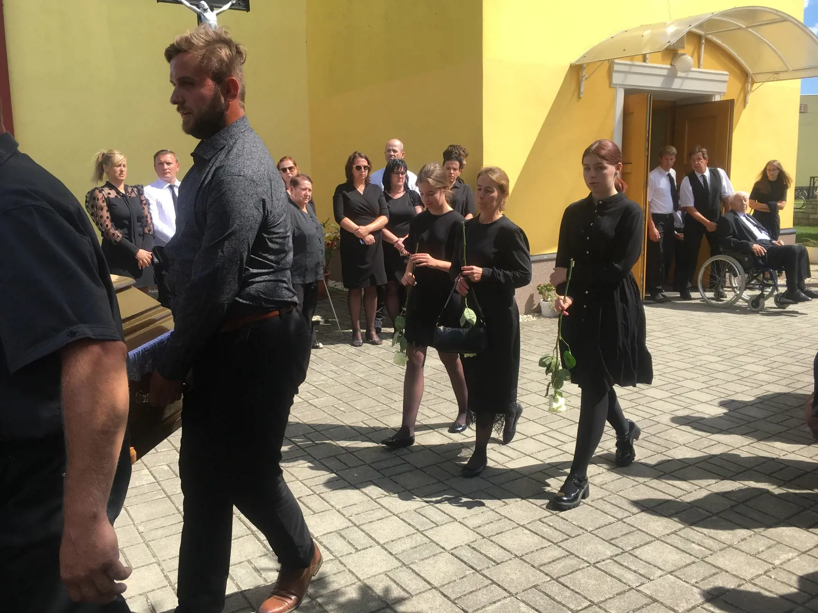 Vdova s dcérami niesli v rukách biele ruže, ktoré dali otcovi a manželovi do hrobu. Z kostola vychádzajú bratia nebohého tlačiac otca Františka na invalidnom vozíku.