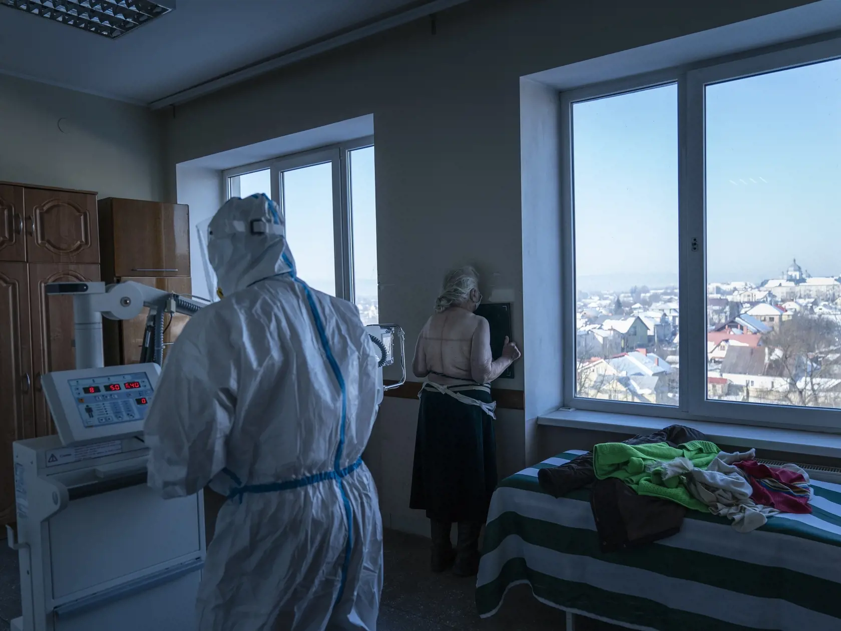 WA 31 Kolomija - Zdravotný pracovník v špeciálnom ochrannom odeve (chrbtom) pripravuje poacientku s ochorením COVID-19 na röntgen pľúc v nemocnici v meste Kolomija na západe Ukrajiny v utorok 23. februára 2021. Na Ukrajinu v utorok dorazili prvé dávky vakcíny proti koronavírusu spôsobujúcemu ochorenie COVID-19. Krajina získala 500.000 dávok vakcíny od spoločnosti AstraZeneca vyrobených v Indii. Prvú dodávku vakcín na Ukrajinu predtým viackrát odložili. FOTO TASR/AP

A medic wearing a special sui