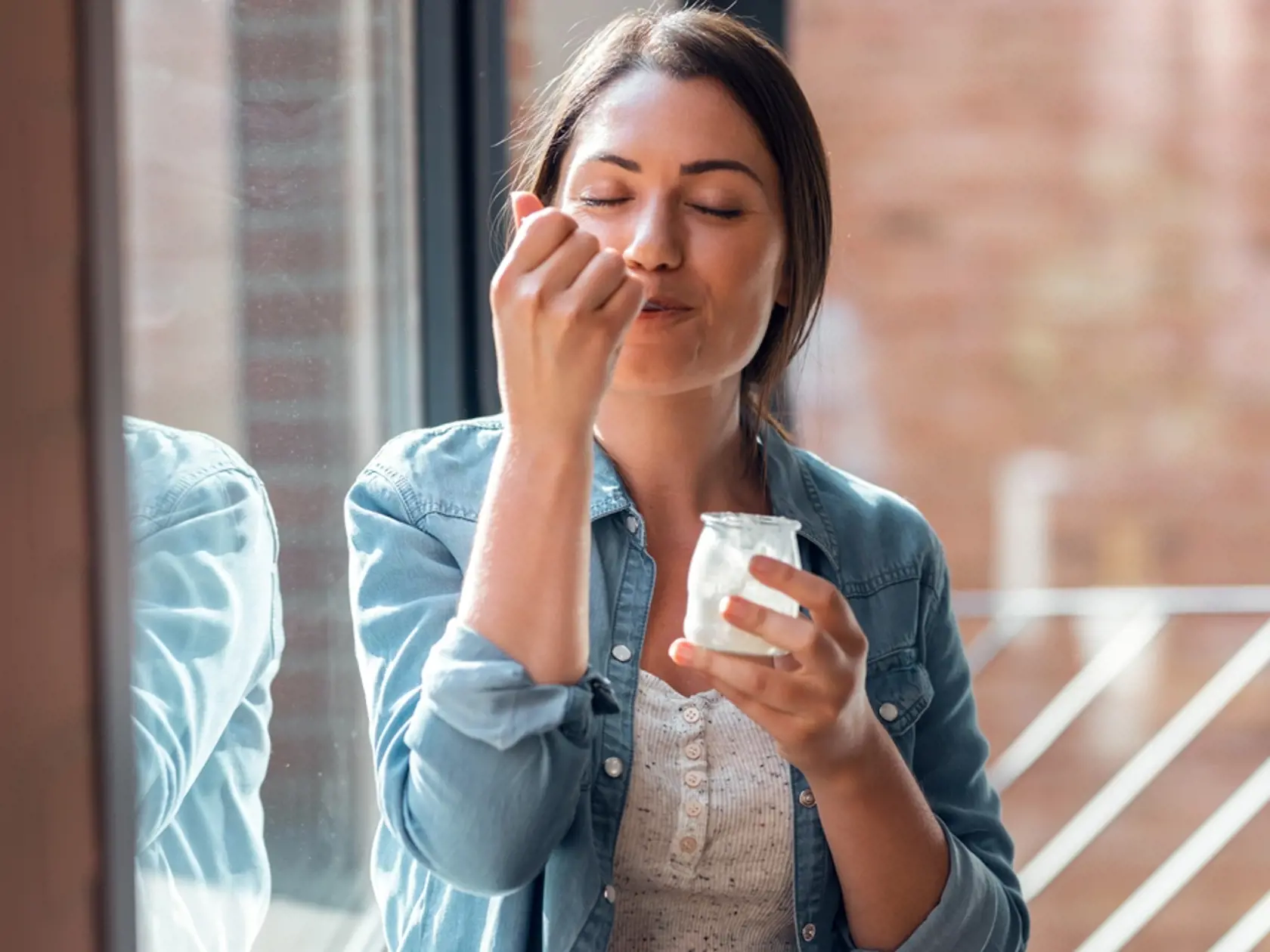 Shot,Of,Happy,Beautiful,Woman,Eating,Yogurt,While,Standing,In