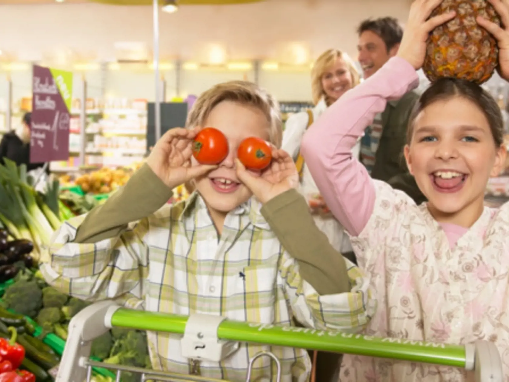 Brother and sister (8-10) playing with fruit in supermarket, smiling