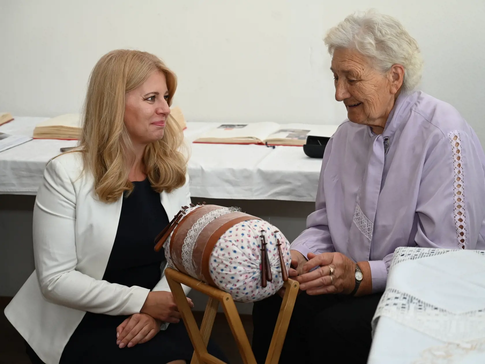 Na snímke vľavo prezidentka SR Zuzana Čaputová sa rozpráva s klientkou, ktorá jej ukazuje čipkovanie v Dennom centre seniorov v Brezovej pod Bradlom počas návštevy myjavského regiónu vo štvrtok 25. augusta 2022. FOTO TASR - Lukáš Grinaj 
