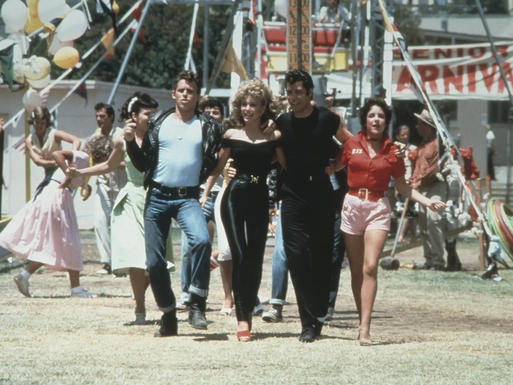 1978:  Left to right: actors Jeff Conaway, Olivia Newton-John, John Travolta and Stockard Channing walk arm in arm at a carnival in a still from the film, 'Grease' directed by Randal Kleiser.  (Photo by Paramount Pictures/Fotos International/Getty Images)