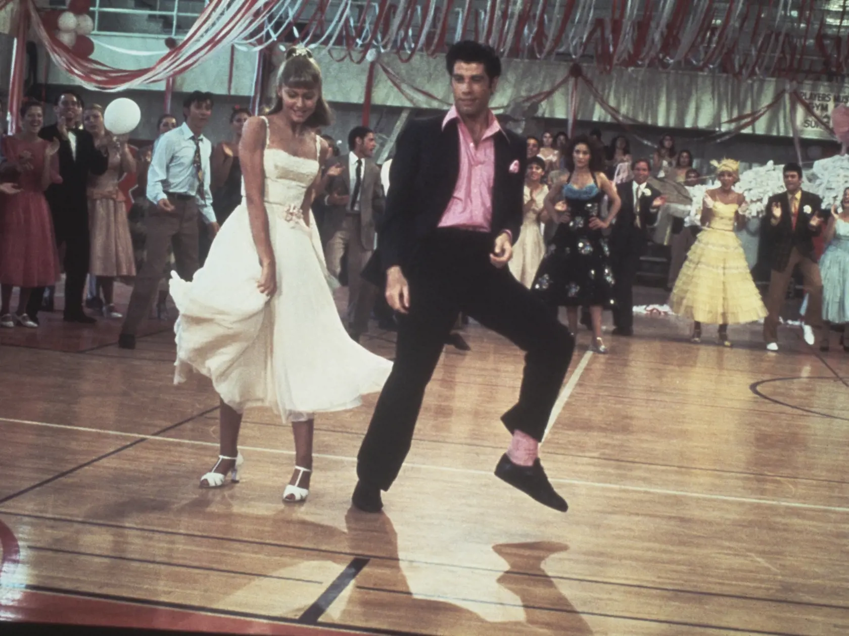 Australian singer and actress Olivia Newton-John and American actor John Travolta dance in a crowded high school gym in a still from the Paramount film, 'Grease', 1978. (Photo by Paramount Pictures/Fotos International/Getty Images)